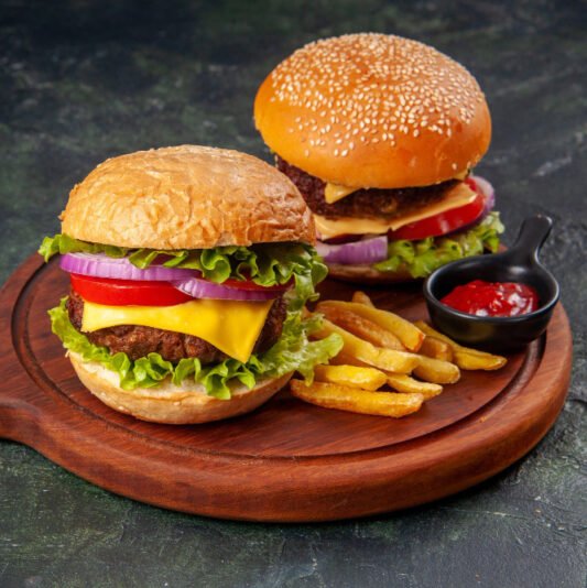 two tasty burgers behind fries on wooden board