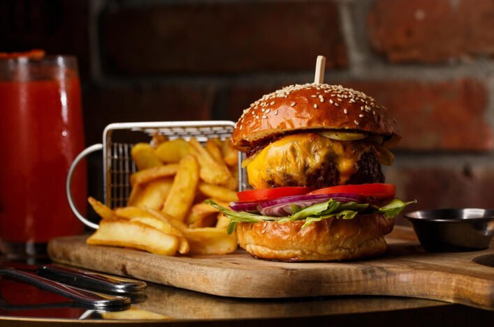 Big delicious Cheeseburger behind thick fries on wooden board